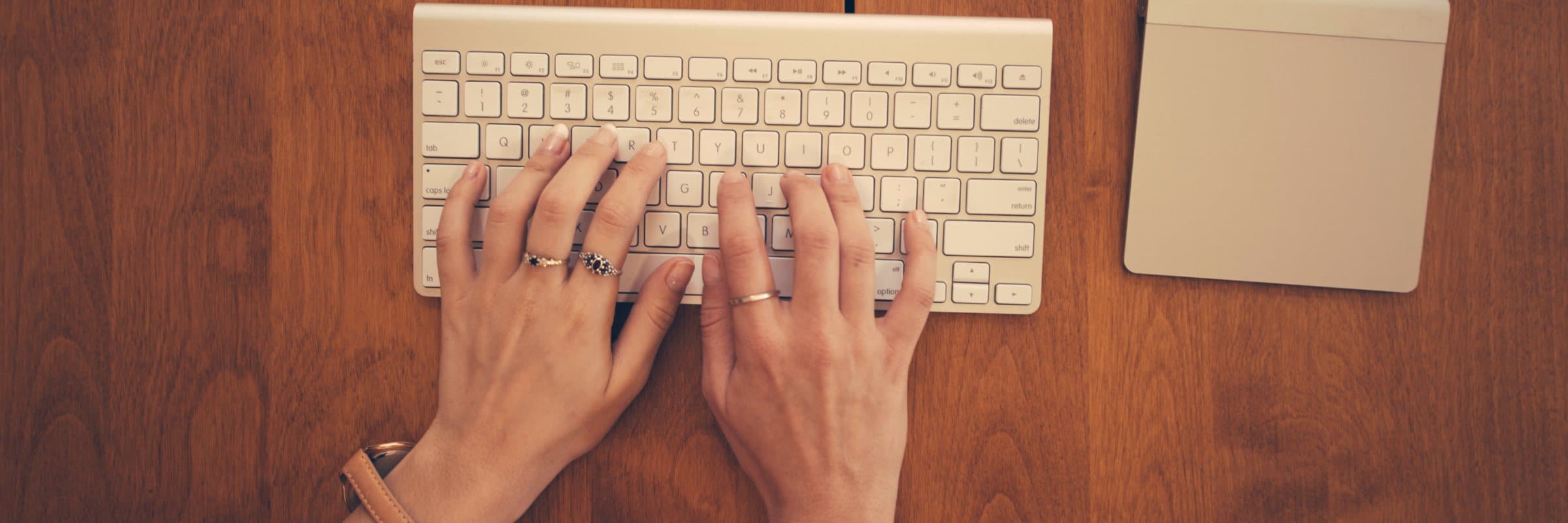 Two hands resting on a keyboard on a wooden desk